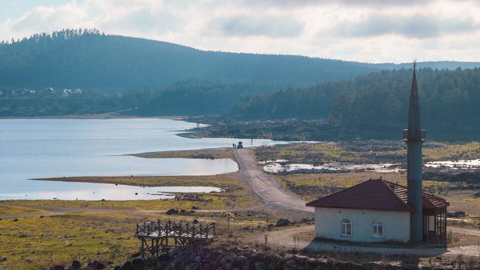 A lake, a wooden structure, a church, and a forested hill.
