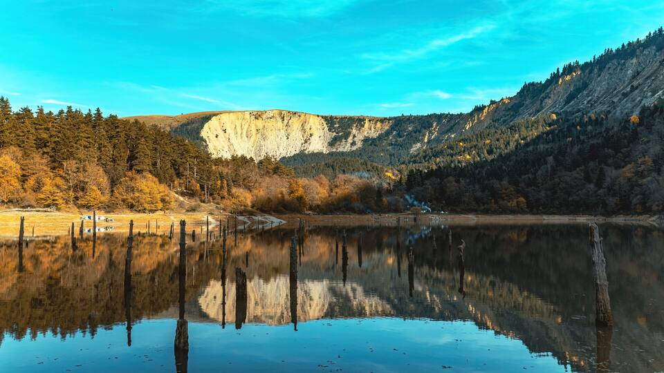 A calm lake with reflections of trees and a cliff.