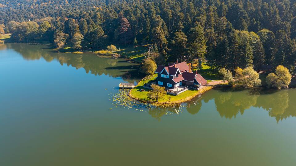A house on a small island surrounded by a lake and dense forest.