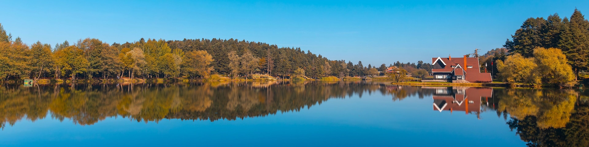 A calm lake with a clear reflection of trees and a house on the right.