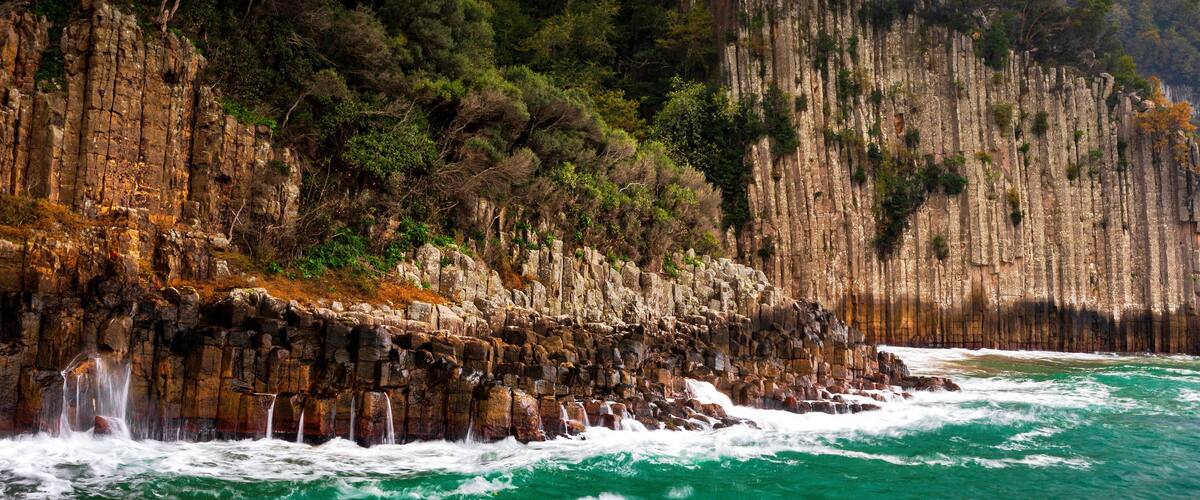 A coastal cliff with a waterfall and turquoise sea.