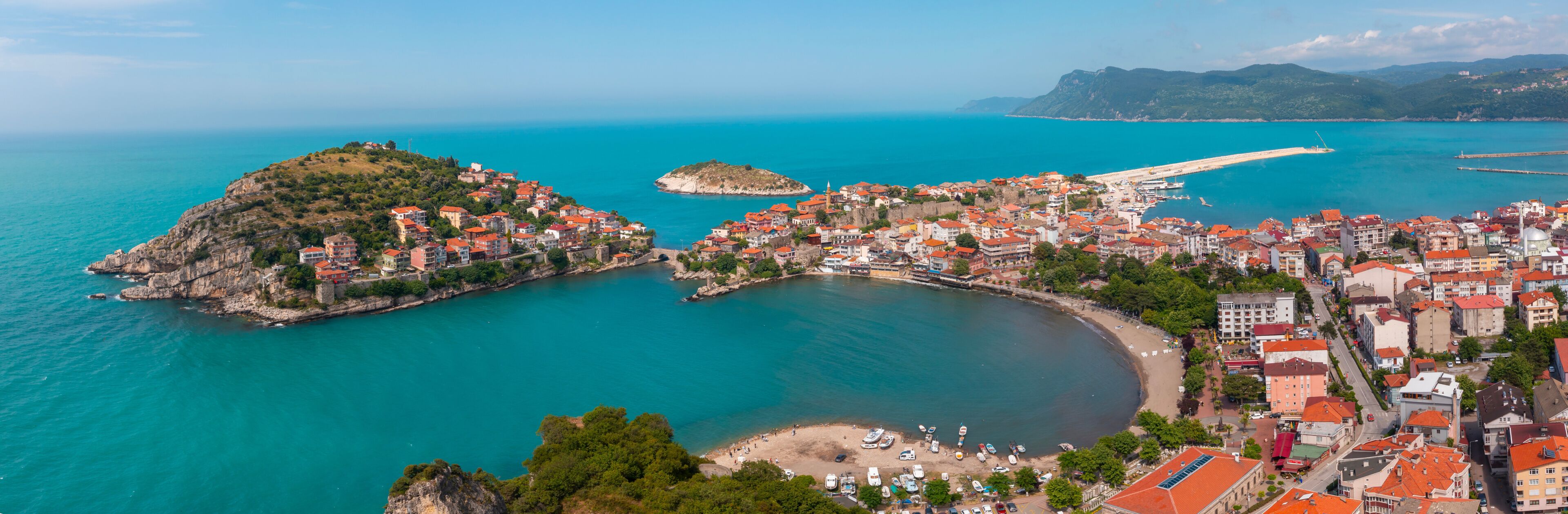 A coastal town with a prominent hill, a bay, and a pier extending into the sea.