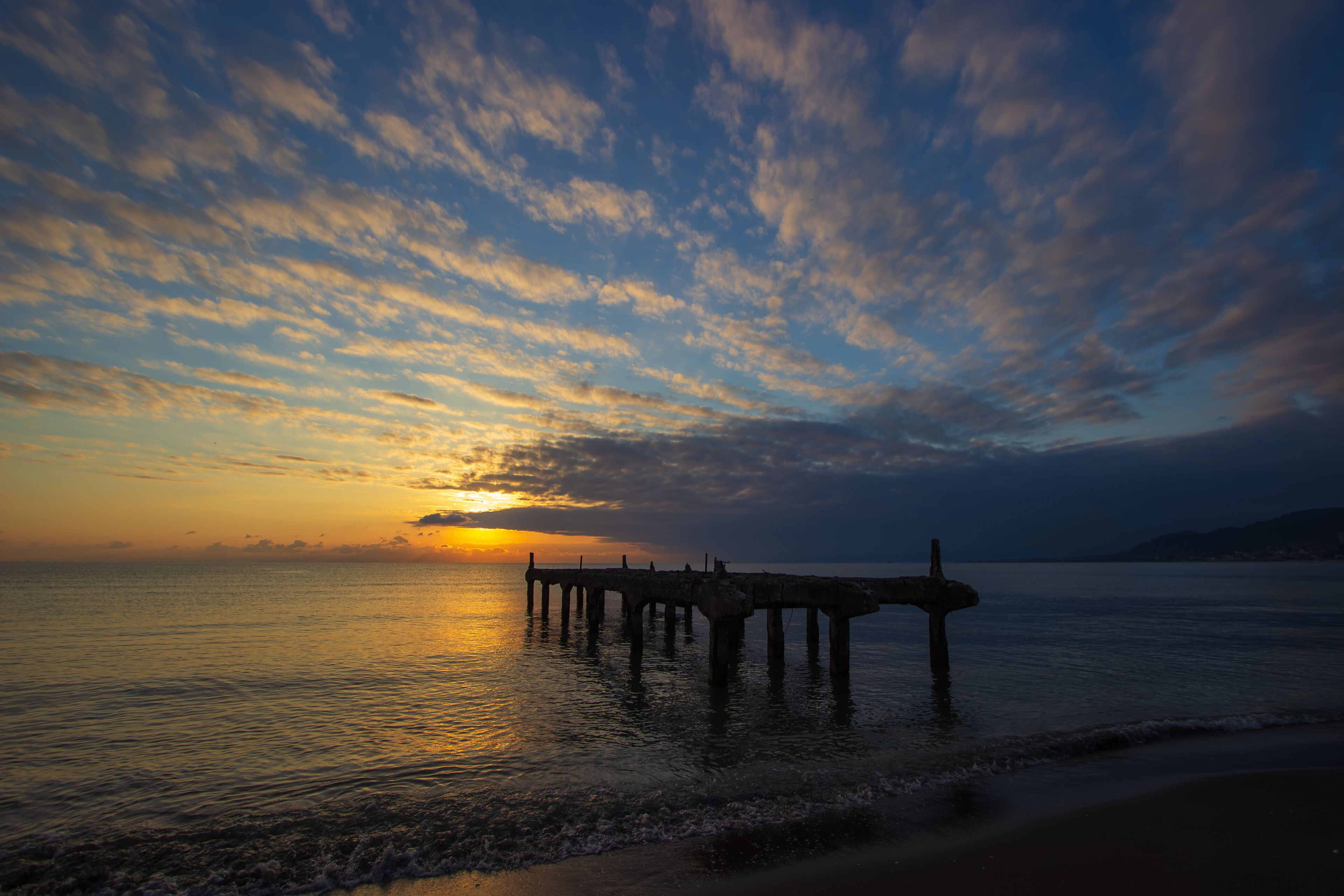 A sunset over a calm sea with a pier extending into the water.
