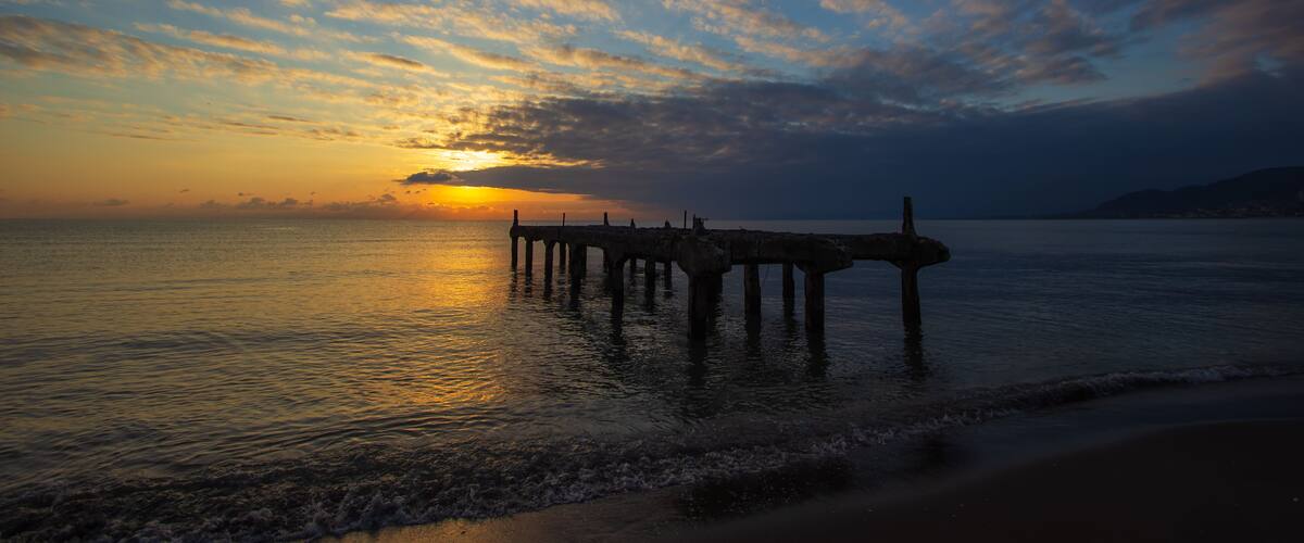 A sunset over a calm sea with a pier extending into the water.