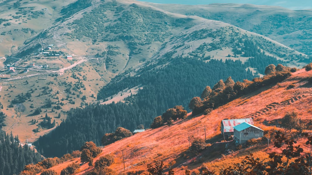 A mountainous landscape with a small house on a hillside.