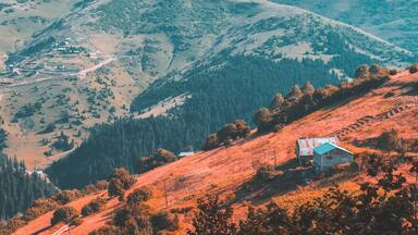 A mountainous landscape with a small house on a hillside.