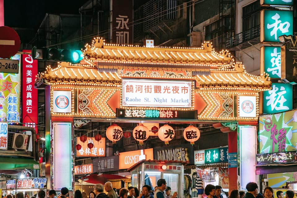 A brightly lit traditional Chinese gate with neon signs and advertisements.