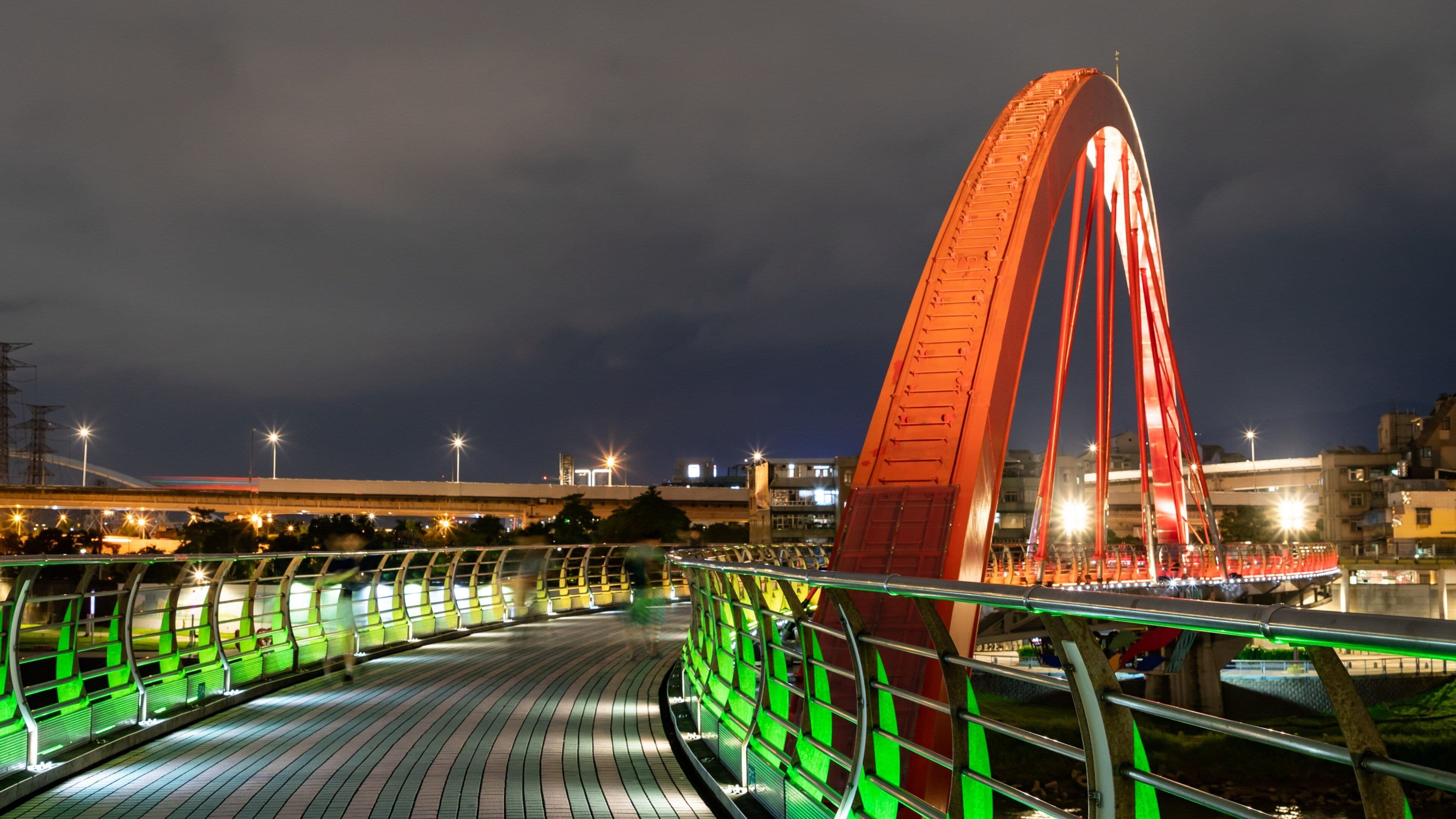 A brightly lit red bridge with green railings at night.