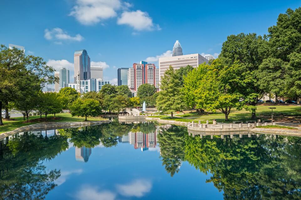 A city skyline with modern skyscrapers and a park with a reflective pond.