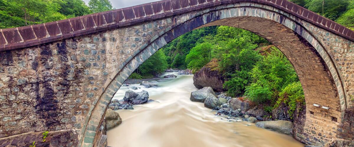 A stone bridge over a river surrounded by lush greenery.
