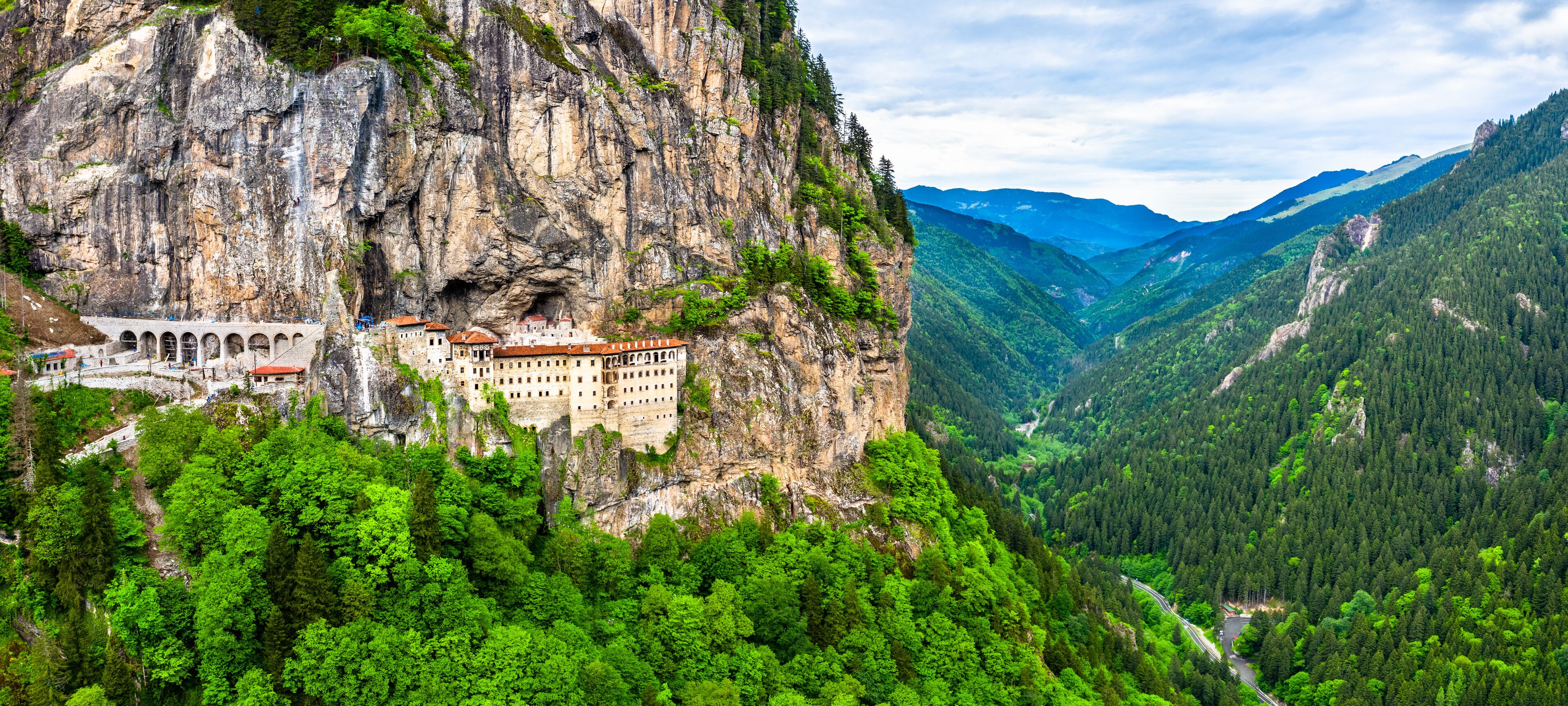 A castle perched on a cliffside, surrounded by lush green forest and mountains.
