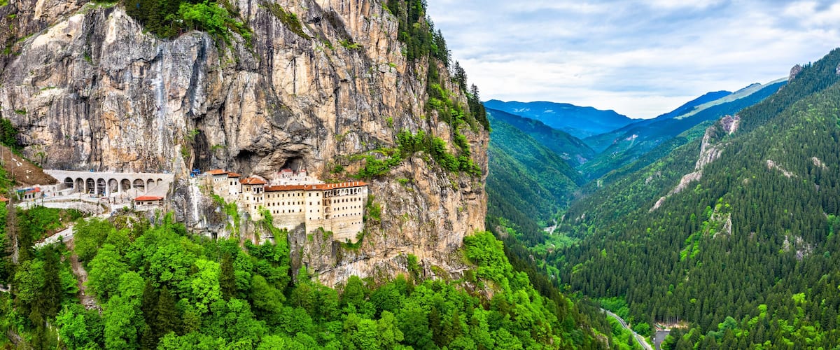 A castle perched on a cliffside, surrounded by lush green forest and mountains.