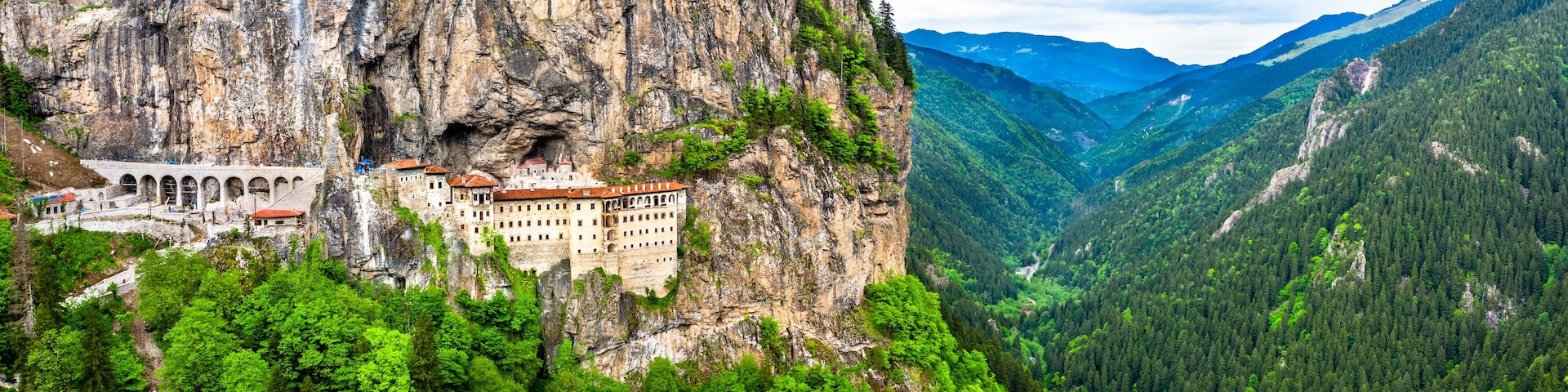 A castle perched on a cliffside, surrounded by lush green forest and mountains.