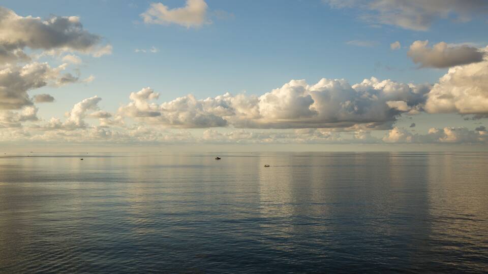 A calm sea with boats and a cloudy sky.