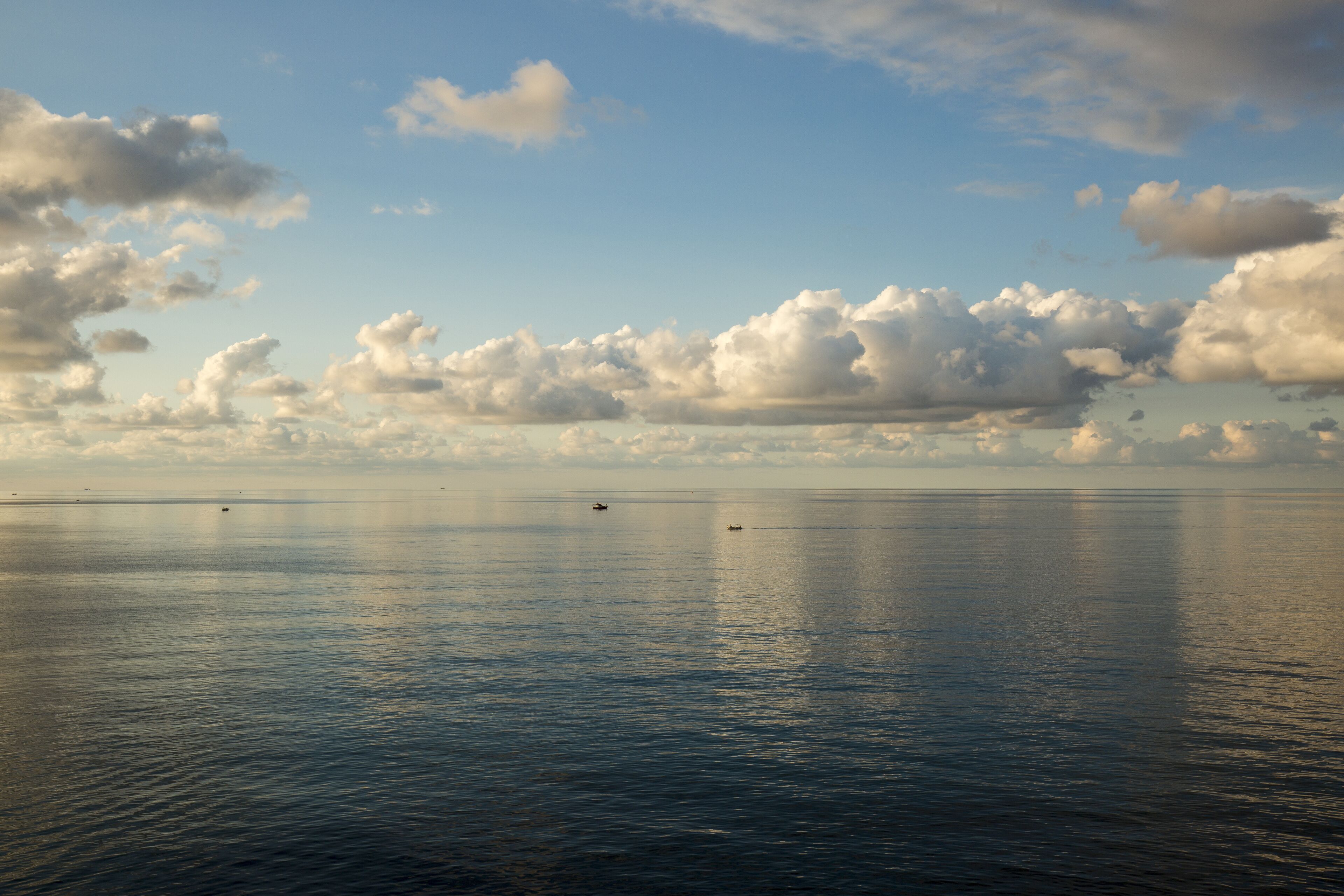 A calm sea with boats and a cloudy sky.