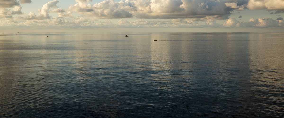 A calm sea with boats and a cloudy sky.
