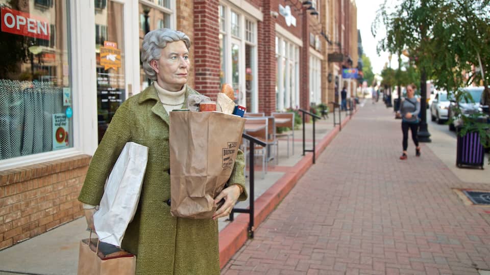 Estátua de uma pessoa segurando sacolas de compras numa calçada.