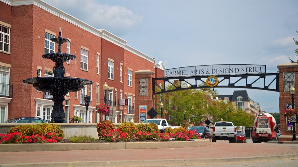A brick building with a fountain, a sign reading "Carmel Arts & Design District," and a street with cars and a truck.