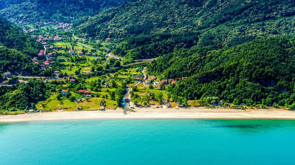 A coastal village with a beach, surrounded by forested hills.