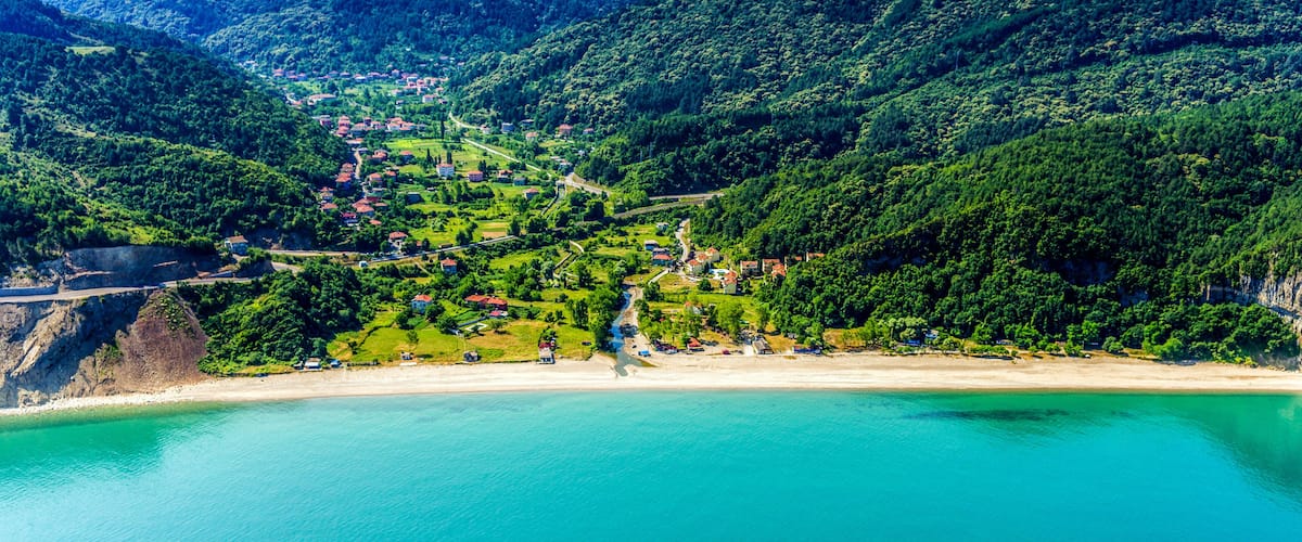 A coastal village with a beach, surrounded by forested hills.