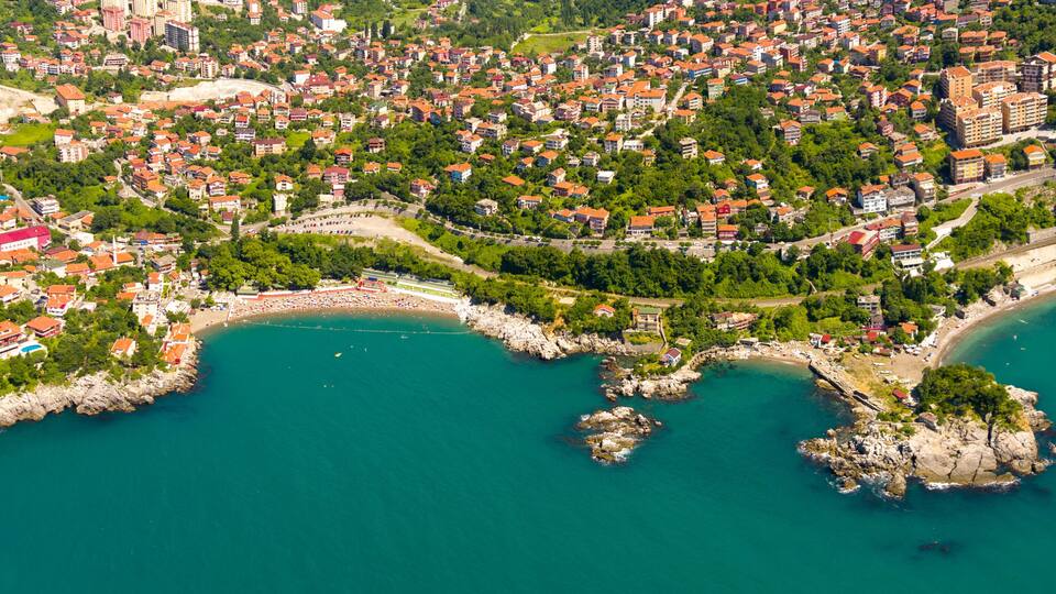 An aerial view of a coastal town with a beach, rocky coastline, and dense residential area.