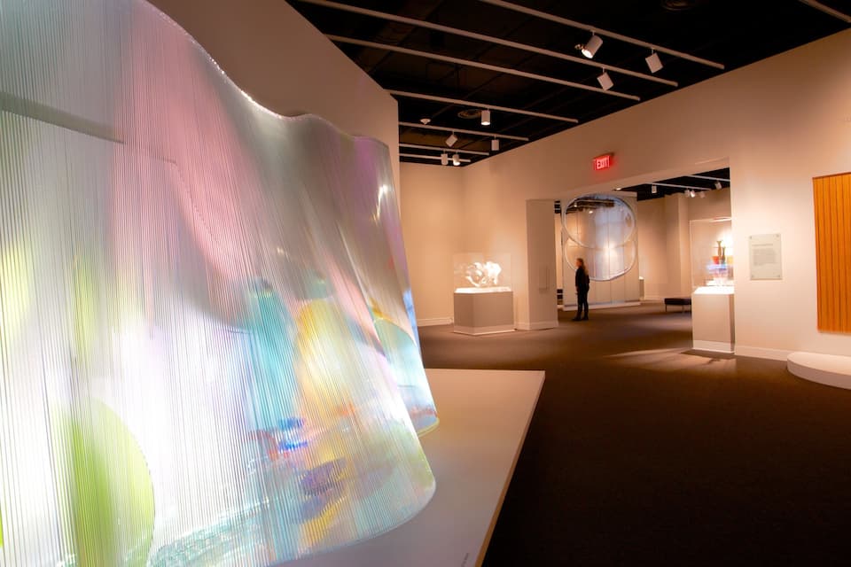 An art gallery with large, colorful installations and a wooden panel on the wall.