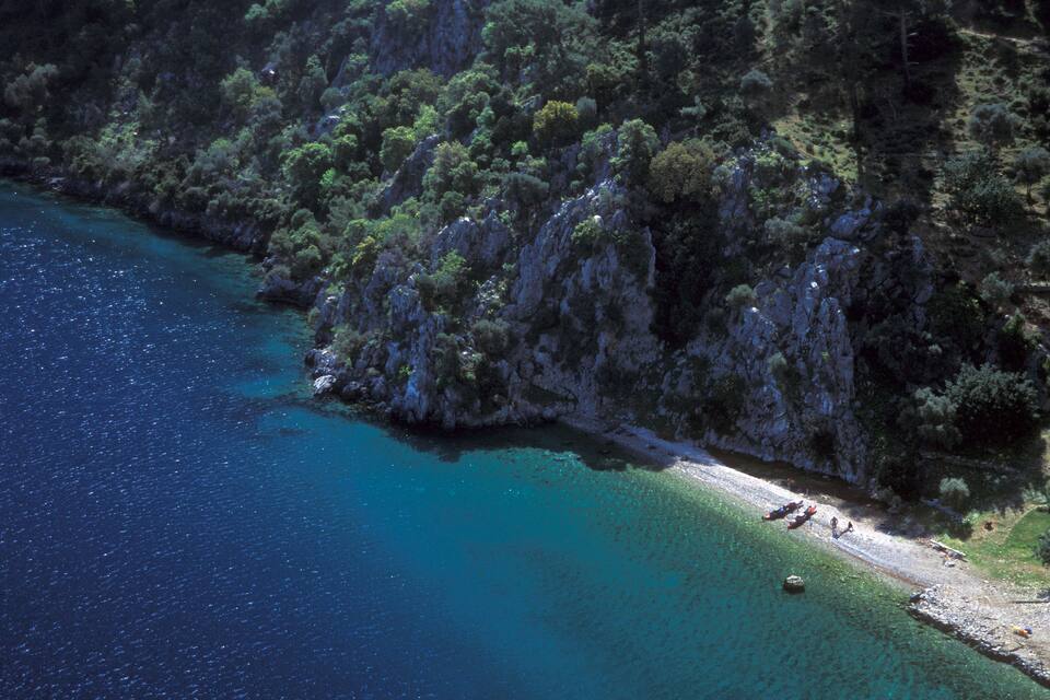 A coastal landscape with clear turquoise waters, rocky cliffs, and dense greenery.
