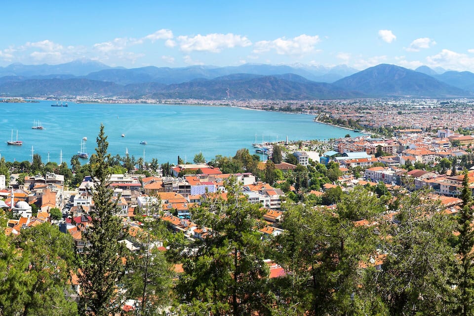 A coastal city with a bay, boats, and mountains in the background.