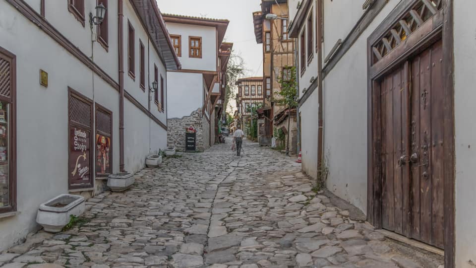 Uma rua de paralelepípedos ladeada por edifícios históricos com persianas de madeira e degraus de pedra.