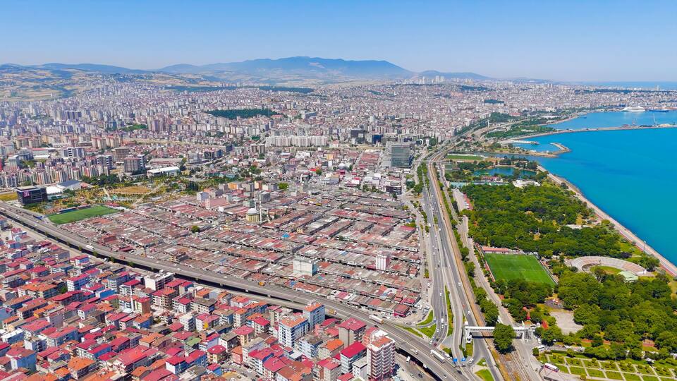A cityscape with a river, green spaces, and mountains in the background.