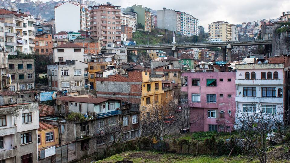 Une zone urbaine densément peuplée, avec des immeubles à plusieurs étages, un pont et une colline en arrière-plan.