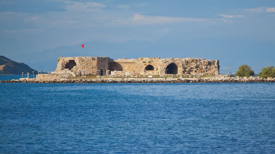 A coastal fort with three arched openings, a red flag atop, and a rocky shoreline.