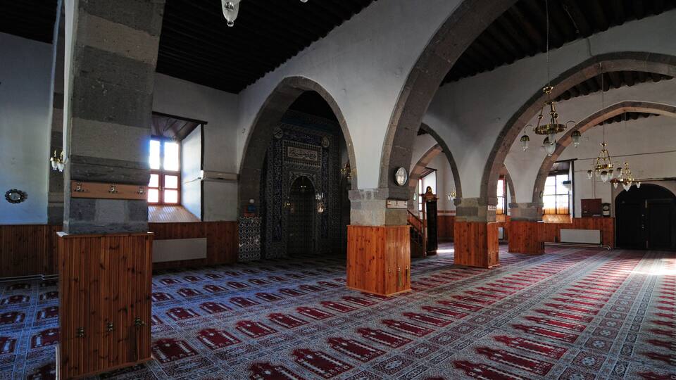 A spacious hall with wooden benches, patterned carpet, and arched ceilings.