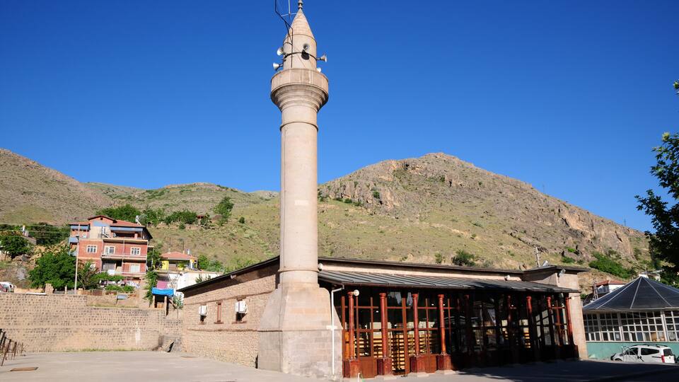 A tall, cylindrical tower with a pointed roof and antennae, surrounded by a building with a metal roof and wooden columns.