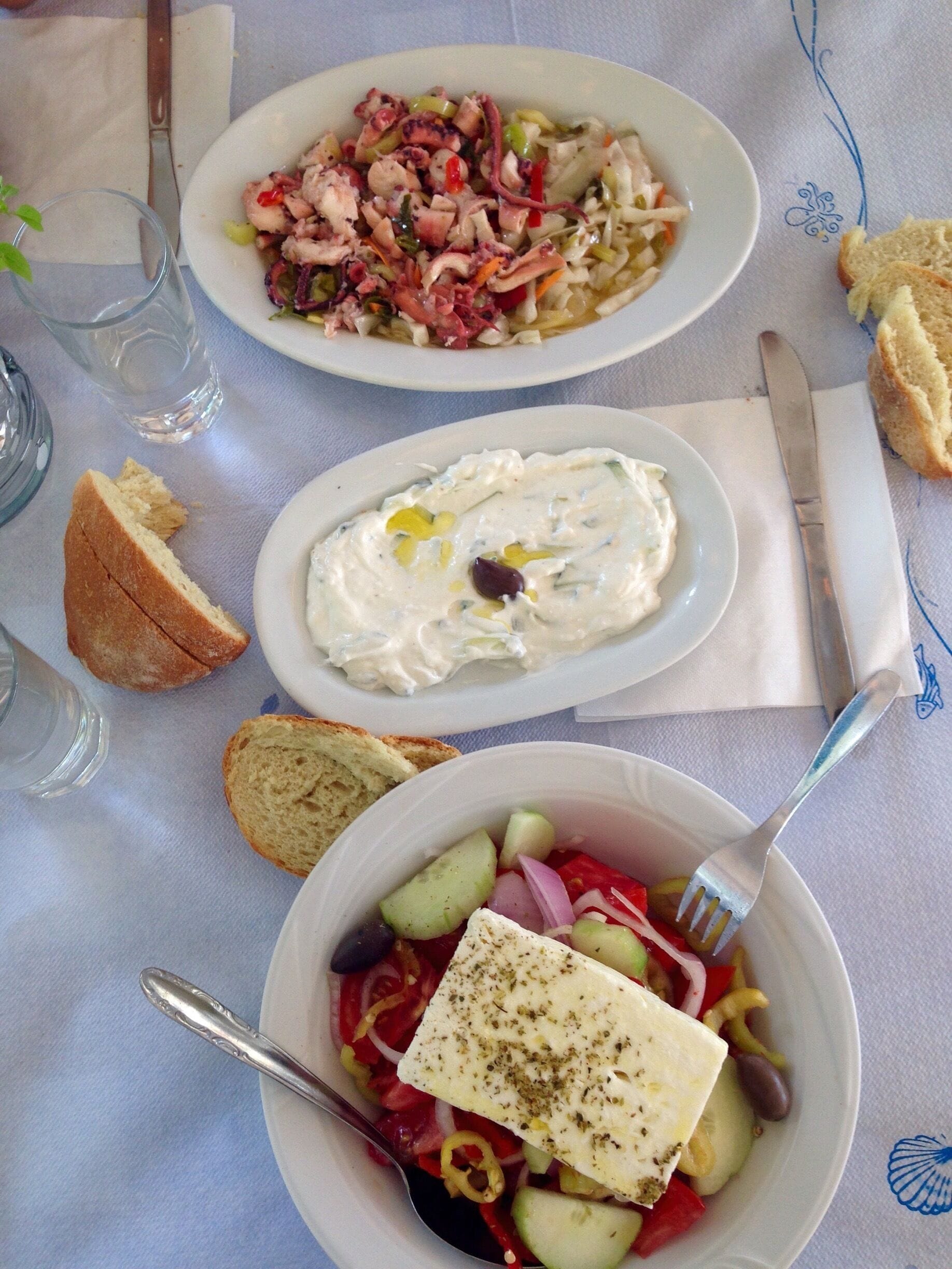 A table with three plates of food, a glass of water, and a knife and fork.