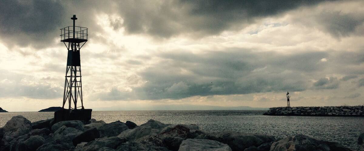 A lighthouse on a rocky shore with a cloudy sky.