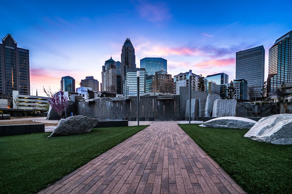 A cityscape with modern skyscrapers, a brick pathway, and large rocks in a landscaped area.