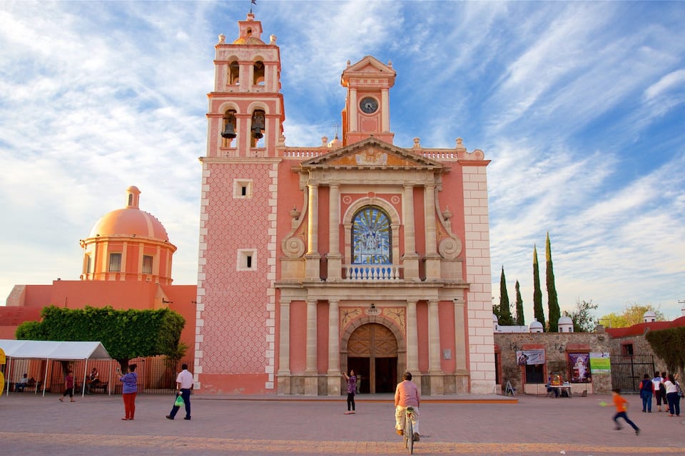 A historic church with a bell tower and dome, surrounded by people and trees.