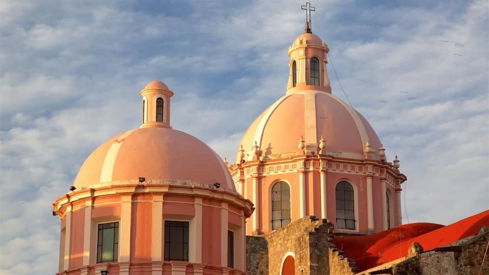 A pink church with two domes and a cross on top.