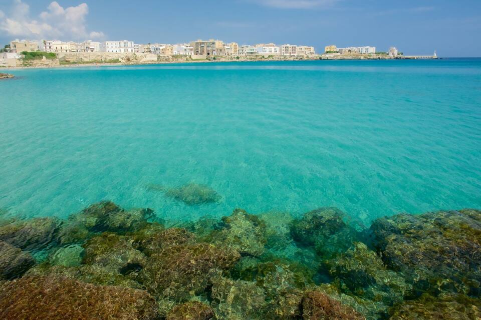 Una cittadina costiera con acque turchesi cristalline, un litorale roccioso e edifici lungo la costa.