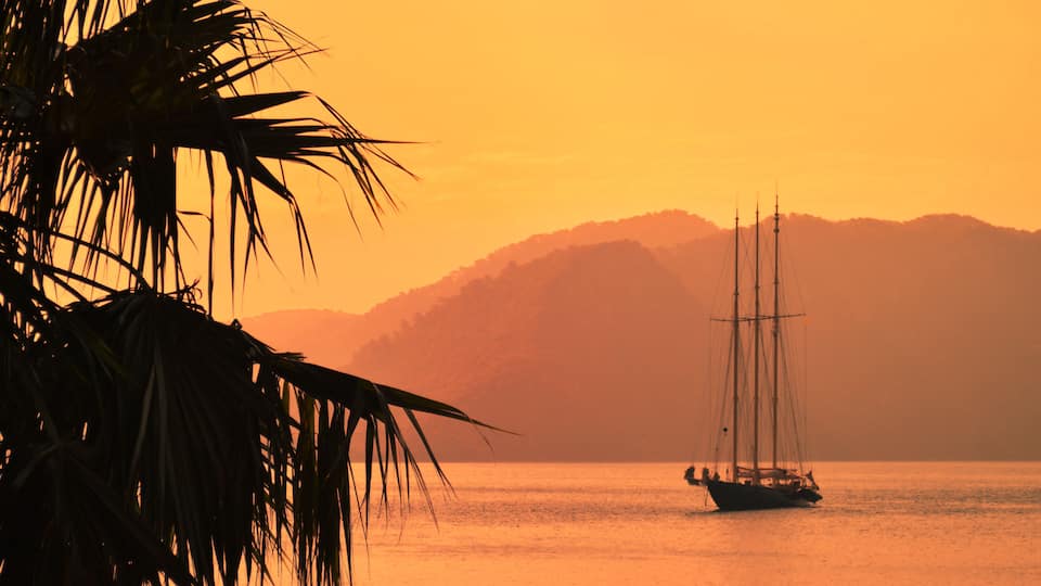 A three-masted sailing vessel in a calm bay in the evening