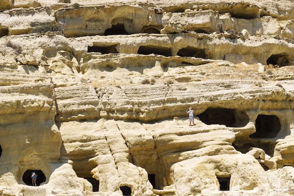 Un paysage rocheux parsemé de nombreuses grottes, et une personne se tenant sur une corniche.