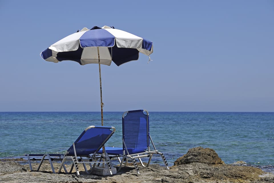 A beach with two blue lounge chairs and a beach umbrella.