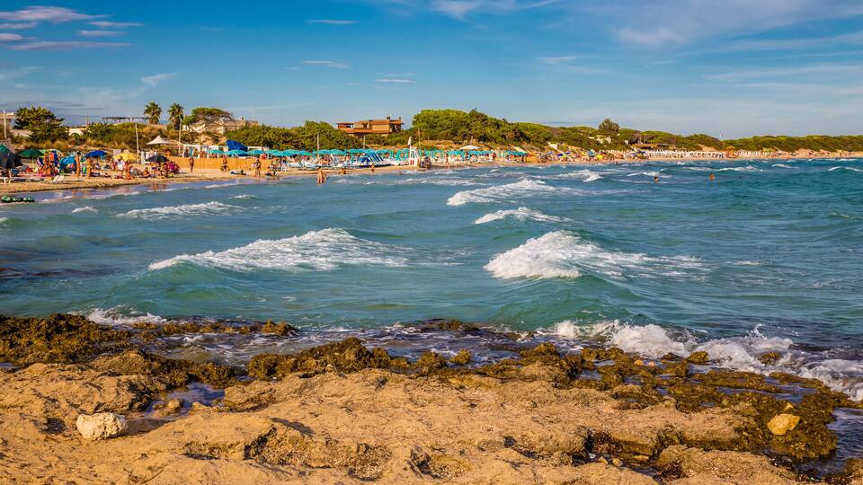 A beach with waves, rocky shore, and beach umbrellas.