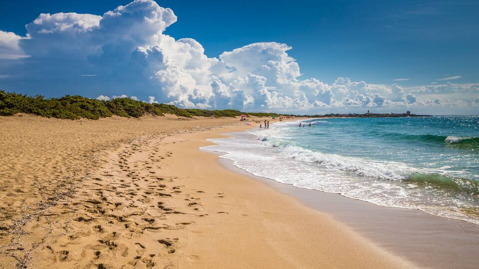 A sandy beach with footprints, a clear blue sky, and waves crashing onto the shore.