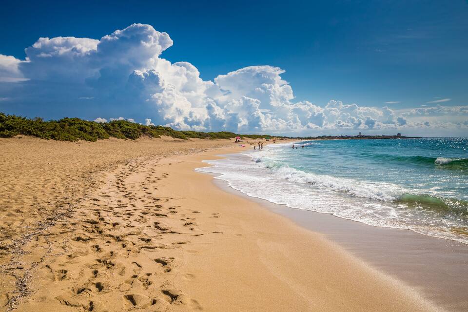 A sandy beach with footprints, a clear blue sky, and waves crashing onto the shore.