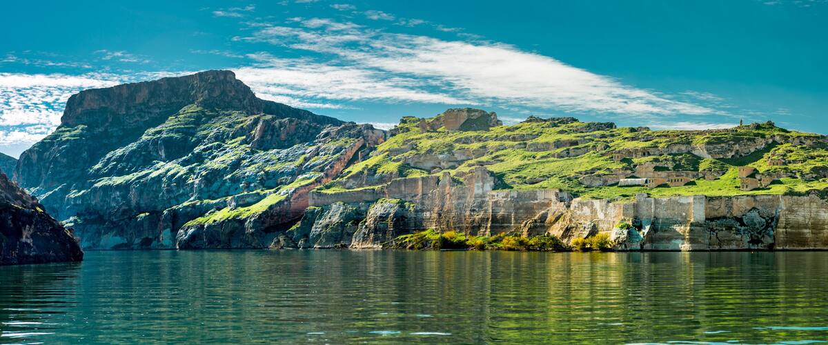 A mountainous landscape with a body of water in the foreground, rocky cliffs, and a small settlement on the hillside.