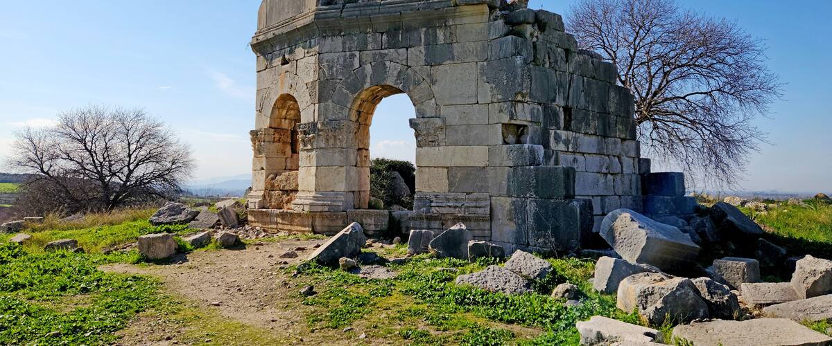 An ancient stone archway with surrounding ruins and a clear sky.
