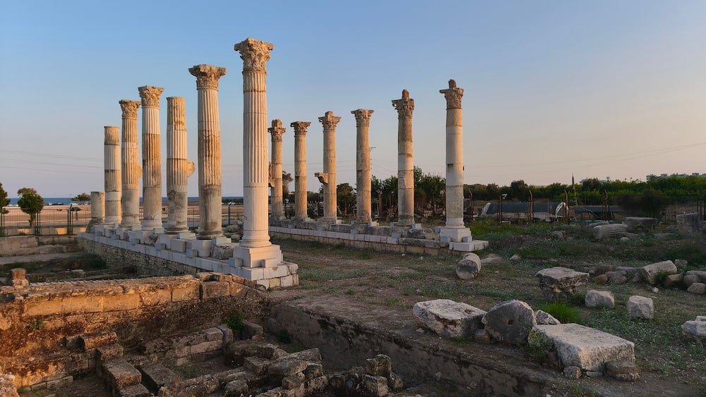Ancient white columns in a ruin, surrounded by stone blocks and a clear sky.
