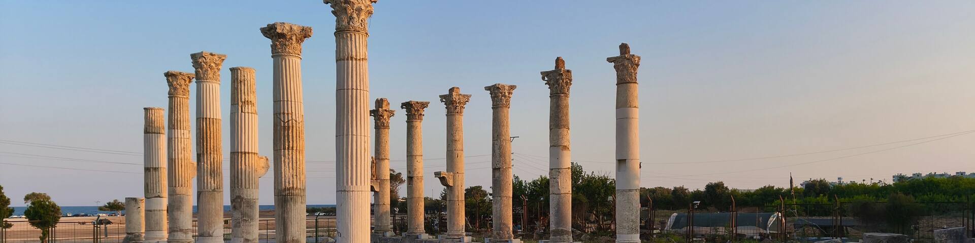 Ancient white columns in a ruin, surrounded by stone blocks and a clear sky.